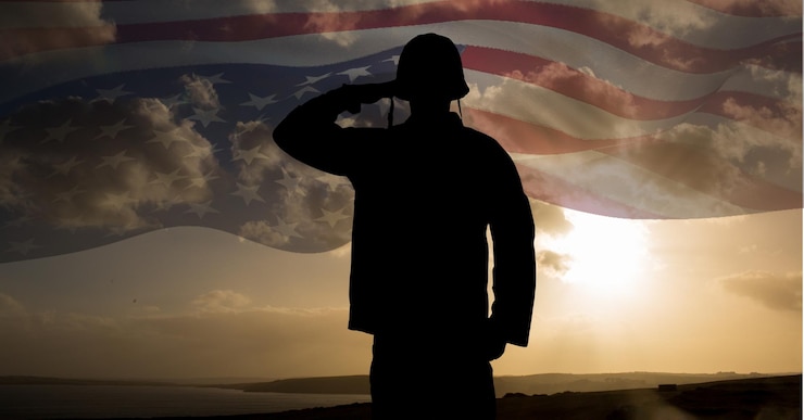 Photo composition of silhouette of saluting soldier against sunset sky with billowing american flag
