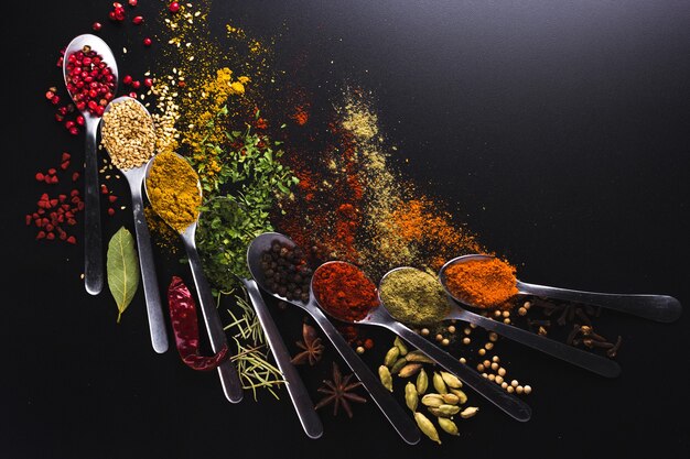 Composition of small spoons full of spices and condiments for cooking on a black background