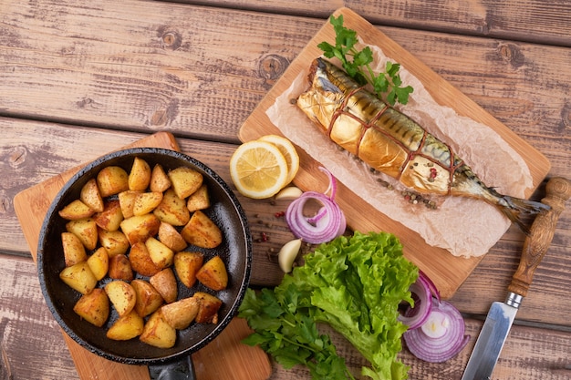 Composition smoked mackerel fish with garnish potatoes lemon greens onions served on wooden board plate top view