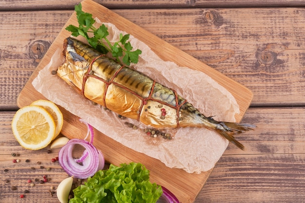 Composition smoked mackerel fish with garnish potatoes lemon greens onions served on wooden board plate top view