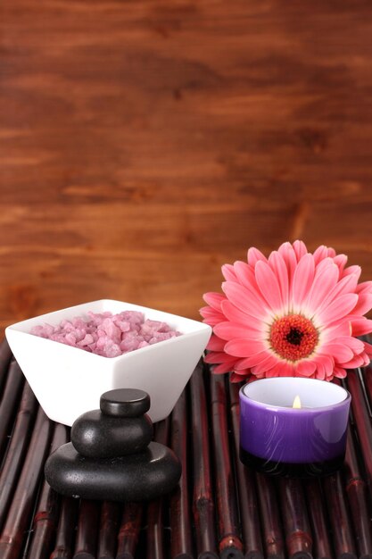 Foto composizione della candela del sale da bagno delle pietre della stazione termale e della gerbera sulla stuoia di bambù su fondo di legno