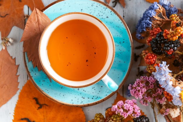 Composition still life of a mug with hot leaf tea with berries and autumn leaves on a wooden surface