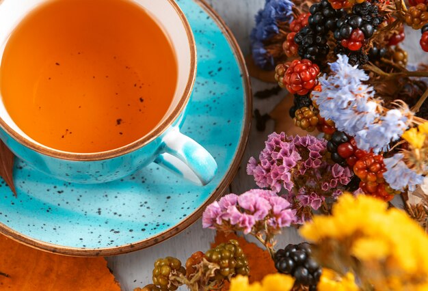 Composition still life of a mug with hot leaf tea with berries and autumn leaves on a wooden surface