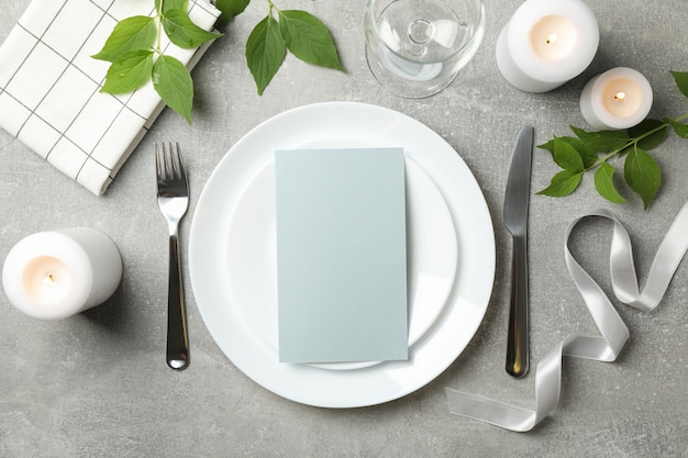 Composition of table setting with candles, leaves and cutlery on gray