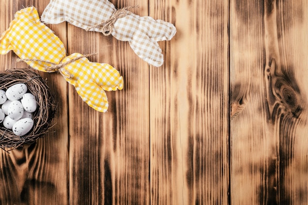 Composizione di due coniglietti quadrati marroni e gialli colorati fatti a mano con foulard su sfondo naturale in legno e uova di quaglia macchiate bianche nel nido di uccelli celebrare le vacanze di pasqua spazio di copia