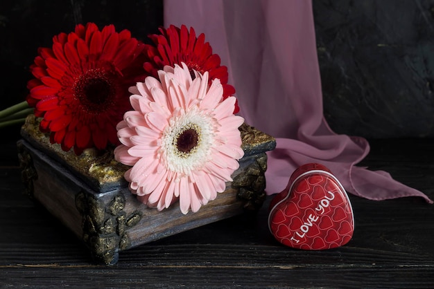 Композиция на День святого Валентина, Женский день или день рождения. Романтический букет герберы и коробка сладостей в форме сердца на деревянном столе крупным планом.