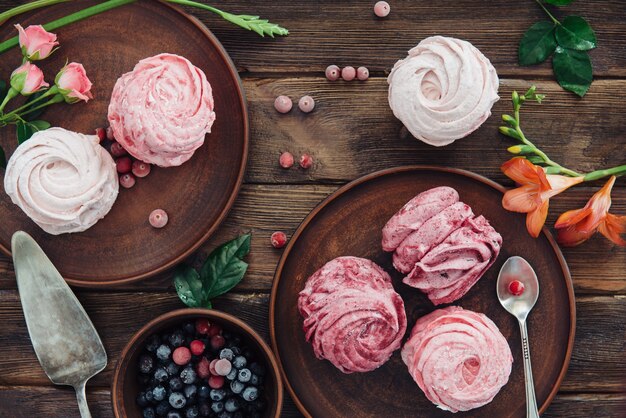 Composition of various blueberry, cherries meringues and flowers on dark wooden surface