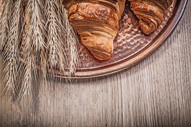 Composition of wheat rye ears freshbaked croissants copper tray on wooden board