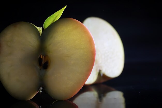 Composition with apple slices on a black background. A slice of apple with back light on a black background with water drops. Juicy apple on a table.