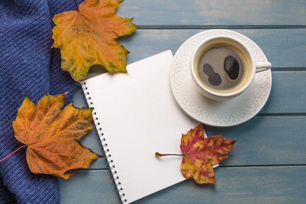 Composition with autumn leaves blank notebooks a cup of coffee on a blue wooden table
