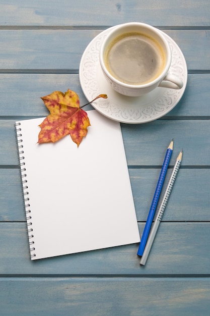 Composition with autumn leaves blank notebooks a cup of coffee on a blue wooden table