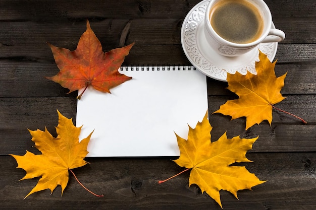 Composition with autumn leaves blank notebooks a cup of coffee on a wooden table