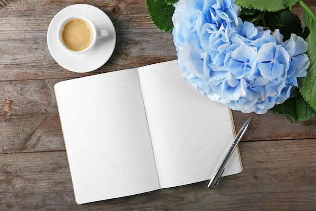 木製の背景に美しい青い花のノートと一杯のコーヒーのコンポジション