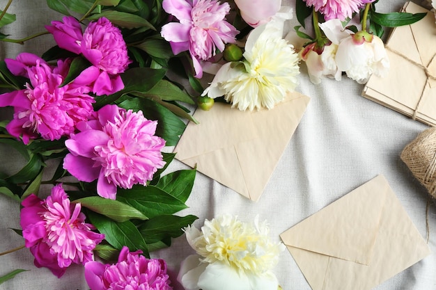 Composition with beautiful peony flowers and envelopes on white fabric top view