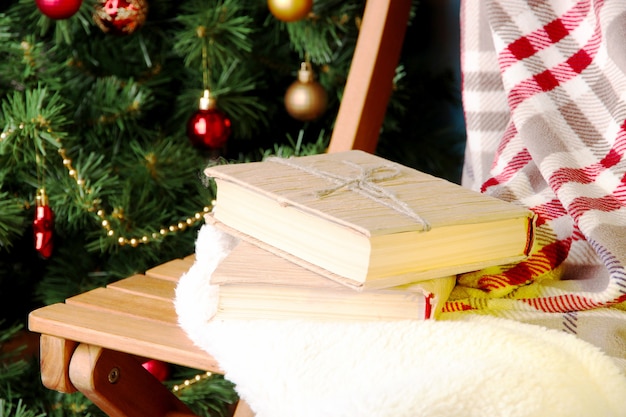 Composition with books and plaid on chair on Christmas tree background