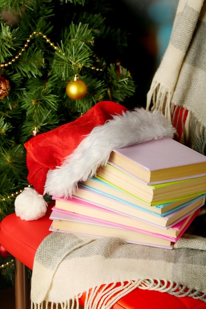 Composition with books and plaid, red hat, on chair on Christmas tree background