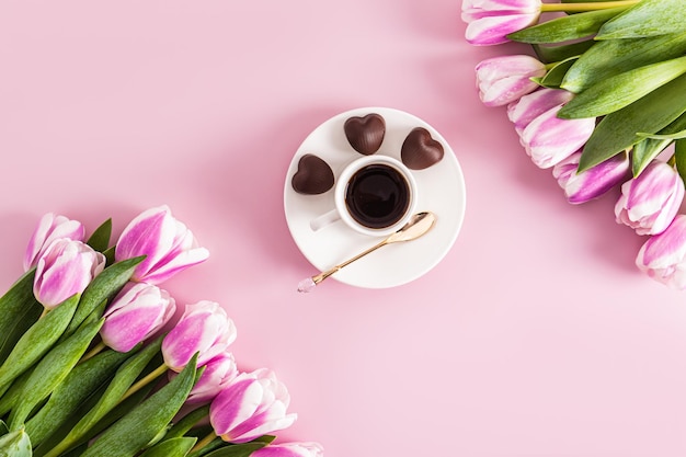 ピンクの背景の上にチューリップの花束とコーヒーのカップを含む構成トップビューフラットレイアウト休日のコンセプト