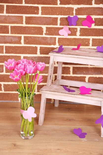 Composition with bouquet of tulips in vase, on ladder, on wall background