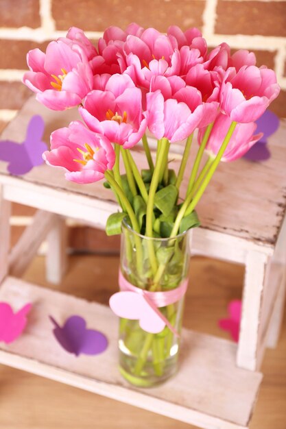 Composition with bouquet of tulips in vase, on ladder, on wall background