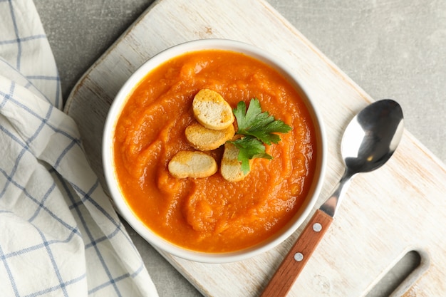 Composition with bowl of pumpkin puree with croutons on gray, top view