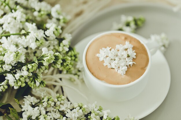 Composition with the branches of lilac and fresh coffee with foam in white cup./