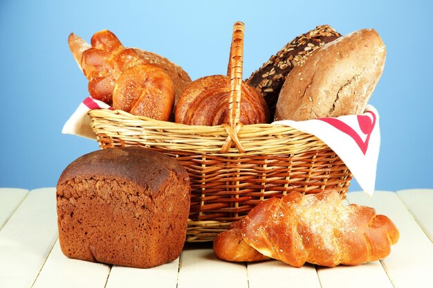 Композиция с хлебом и булочками в плетеной корзине на деревянном столе на цветном фоне