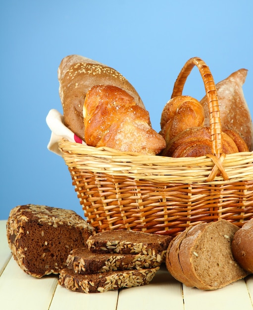 Composition with bread and rolls, in wicker basket on wooden table, on color surface