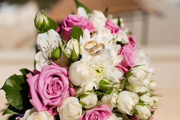 Composition with the bride\'s bouquet of pink roses and wedding\
rings visible from a high angle