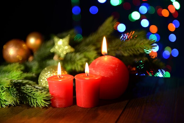 Composition with burning candles, fir tree and Christmas decorations on multicolor lights surface