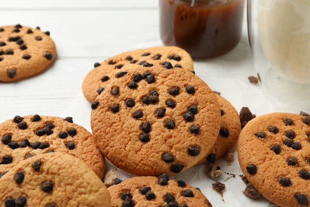 Composition with chip cookies, milk and caramel on white wooden table