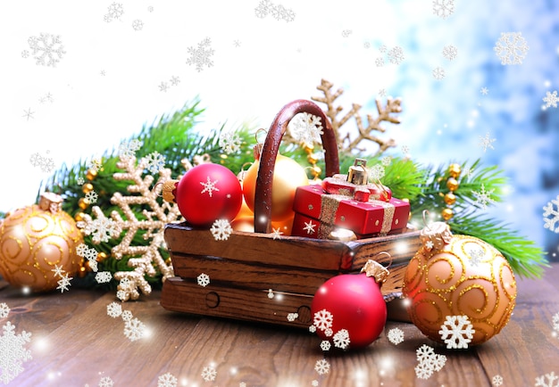 Composition with Christmas decorations in basket, fir tree on wooden table, on light surface