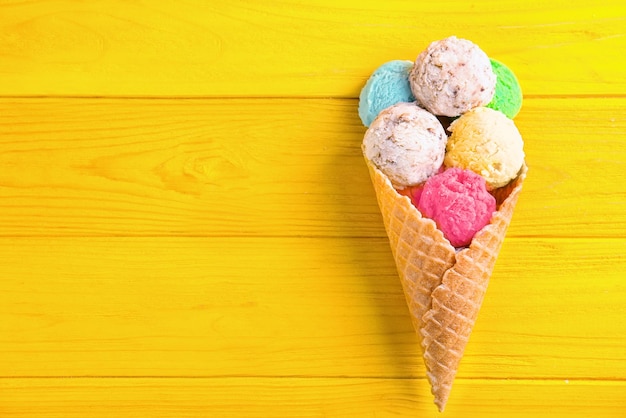 Composition with colorful icecream scoops and waffle cone on wooden background