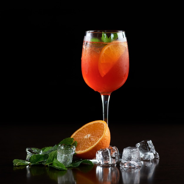 Composition with crystal cocktail glass with cold drink, slice of orange, fresh green mint leaves