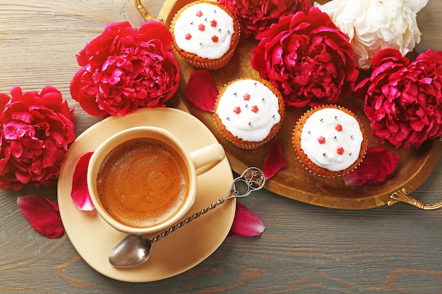 Композиция с чашкой кофе, кексами и цветами пиона на деревянном фоне