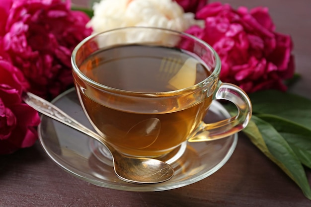 Composition with cup of herbal tea and peony flowers on wooden background