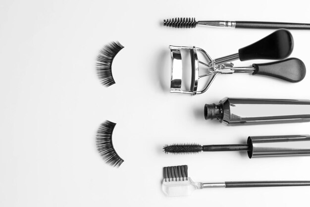 Composition with curler and false eyelashes on white background