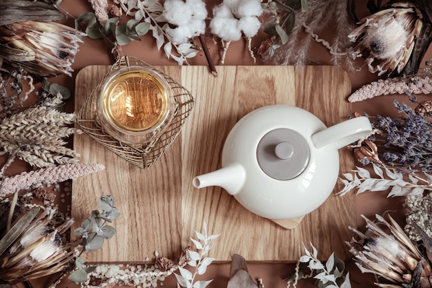 Composition with dry wildflowers and natural herbal tea in a teapot on a wooden surface.