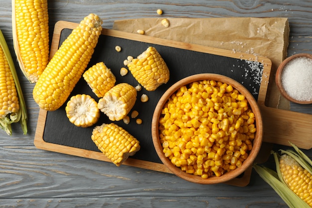 Composition with fresh raw corn and cutting board on wooden table