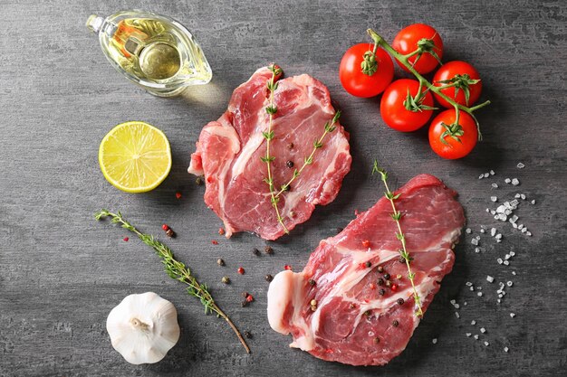 Composition with fresh raw steaks thyme and vegetables on table