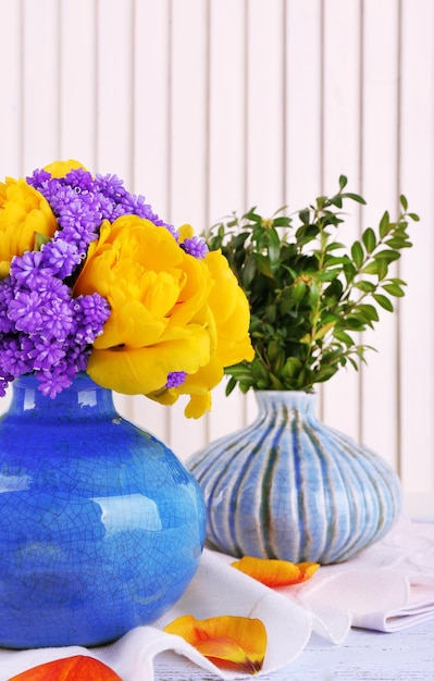 Composition with fresh spring flowers in ceramics vases on wooden background