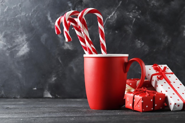 Composition with gifts, sweet candy cane in a cup on color background