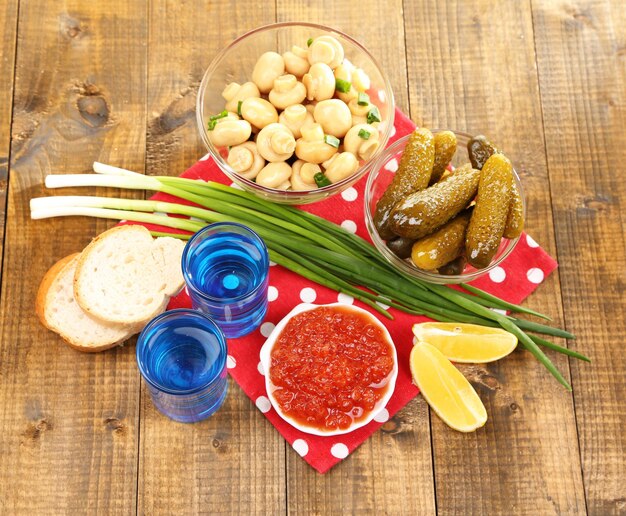 Composition with glass of vodka and marinated mushrooms cucumbers on wooden background