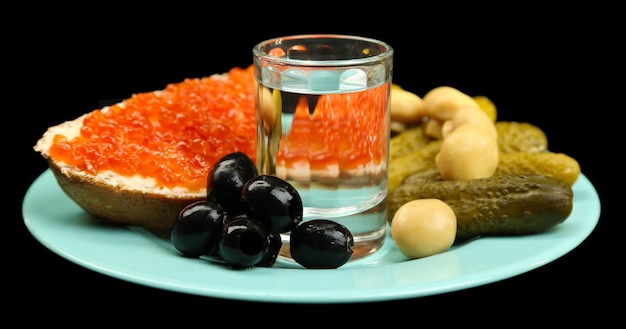 Composition with glass of vodka and snacks on color plate isolated on black