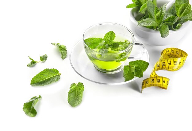 Composition with herbal tea mint leaves and measuring tape on white background Weight loss concept