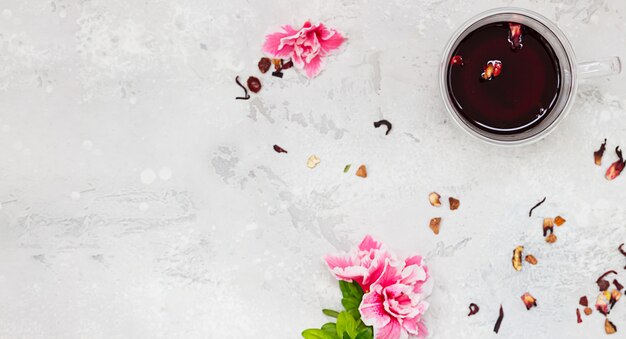 Composition with hot hibiscus tea in glass mug with pink flowers and dry tea leaves. Top view.