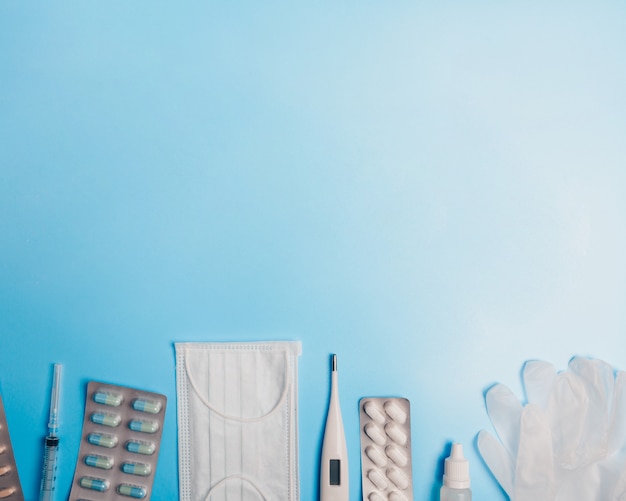 Composition with medical mask, thermometer, syringe, pills and gloves on a blue background. Copyspace.