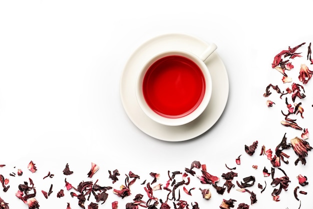 Composition with mug of hibiscus tea and tea petals isolated on white background.