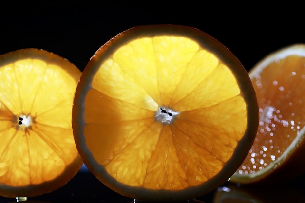 Composition with orange and grapefruit slices on a black background. A slice of orange with back light on a black background with water drops. Juicy orange on a table.