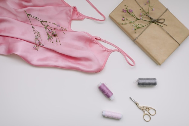 クラフト紙のピンクのシルク生地の贈り物と白い背景の上の糸とはさみで構成フラットレイトップビュー趣味のレジャーコンセプト