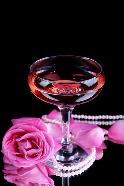 Composition with pink sparkle wine in glass and  rose isolated on black